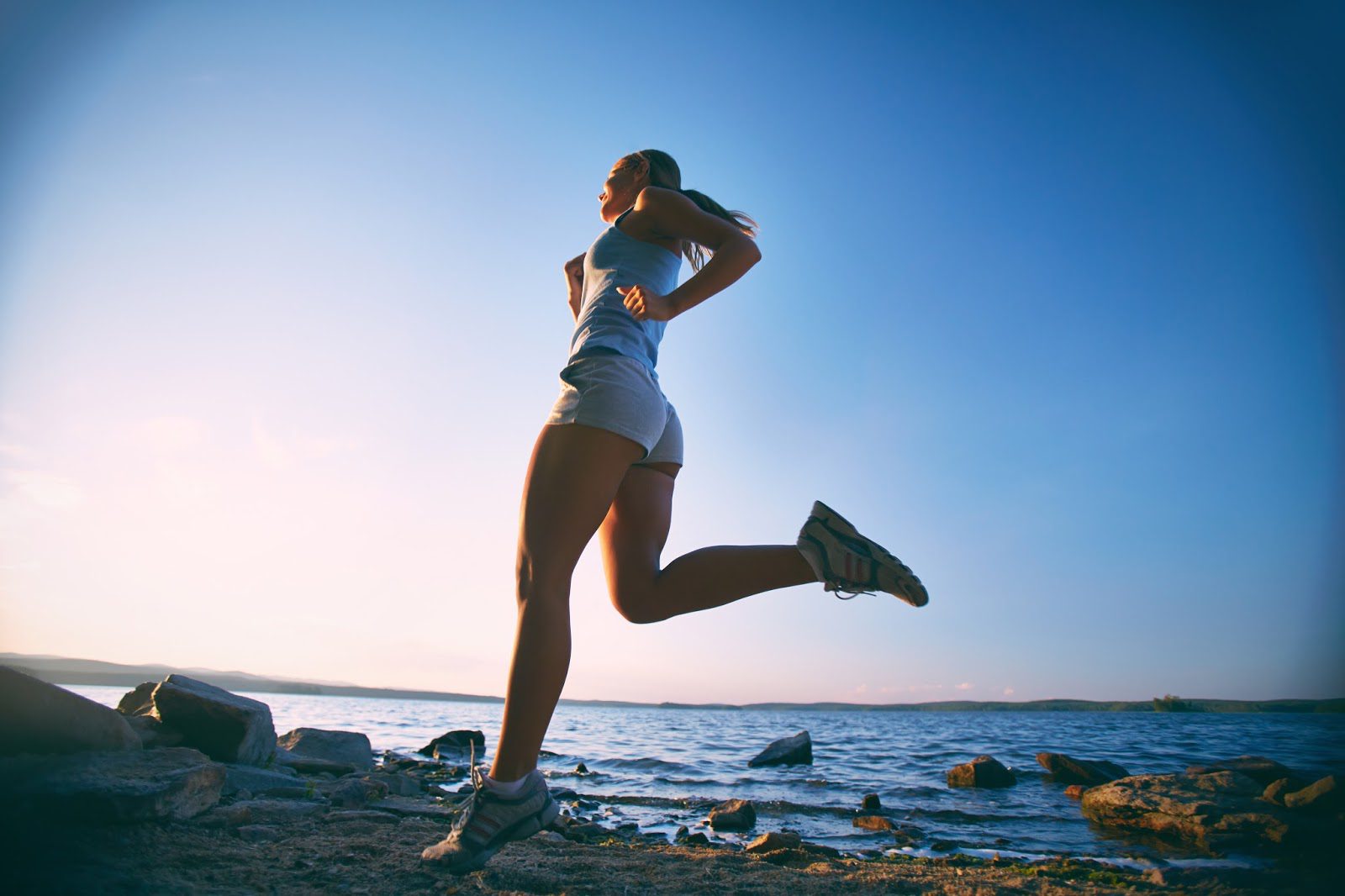 A woman jogging on rocky terrain near the ocean at sunrise.